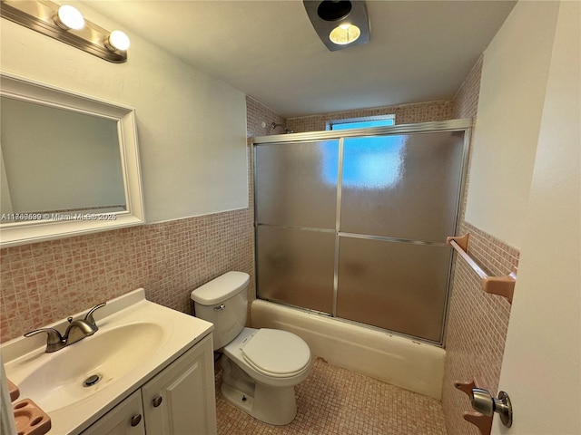 bathroom with tile patterned flooring, toilet, vanity, enclosed tub / shower combo, and tile walls