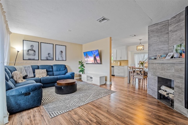 living area with visible vents, a large fireplace, a textured ceiling, and light wood-style flooring