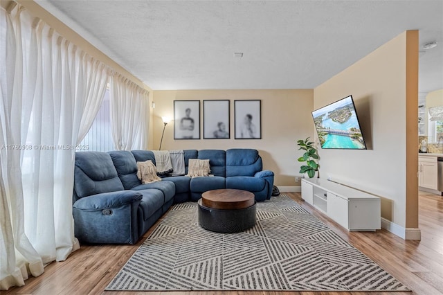 living room with baseboards, light wood-type flooring, and a textured ceiling