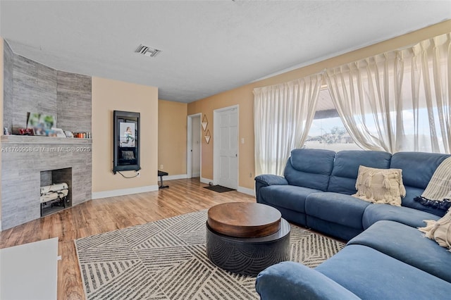 living area featuring wood finished floors, baseboards, visible vents, a tile fireplace, and a textured ceiling