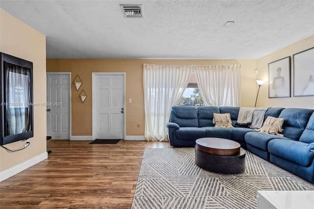 living area with a textured ceiling, wood finished floors, visible vents, and baseboards