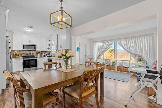 dining room featuring light wood-type flooring, visible vents, and an inviting chandelier