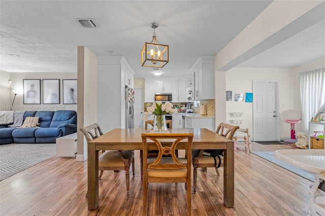 dining area featuring visible vents, light wood-type flooring, and an inviting chandelier