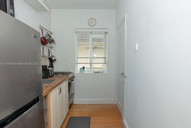 interior space with baseboards, butcher block counters, light wood-type flooring, appliances with stainless steel finishes, and white cabinets