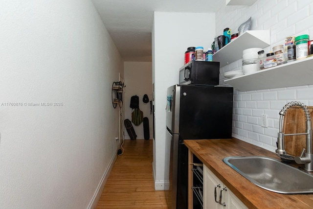 kitchen featuring light wood finished floors, wooden counters, freestanding refrigerator, a sink, and black microwave