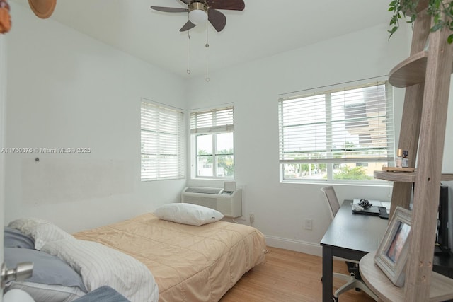 bedroom featuring baseboards, multiple windows, light wood-style floors, and an AC wall unit