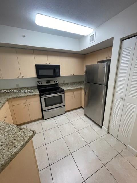 kitchen with light tile patterned floors, visible vents, cream cabinetry, and appliances with stainless steel finishes