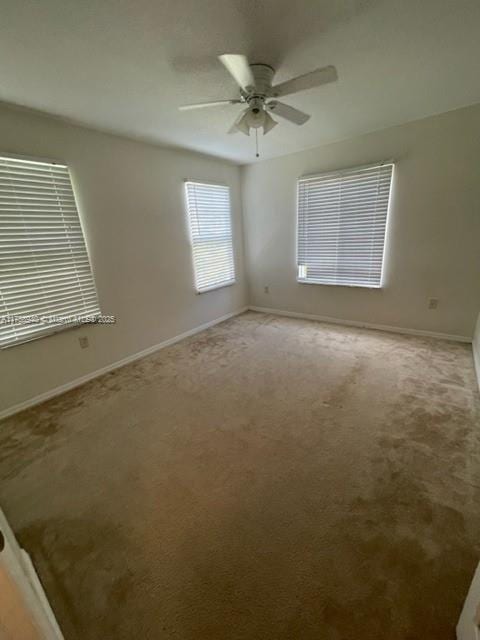 carpeted empty room featuring a ceiling fan and baseboards