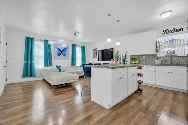 kitchen featuring backsplash, open floor plan, a breakfast bar area, wood finished floors, and stone countertops