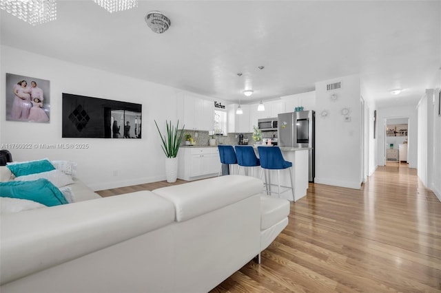 living area featuring baseboards, visible vents, and light wood finished floors