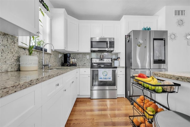 kitchen featuring visible vents, decorative backsplash, light wood-style flooring, appliances with stainless steel finishes, and a sink