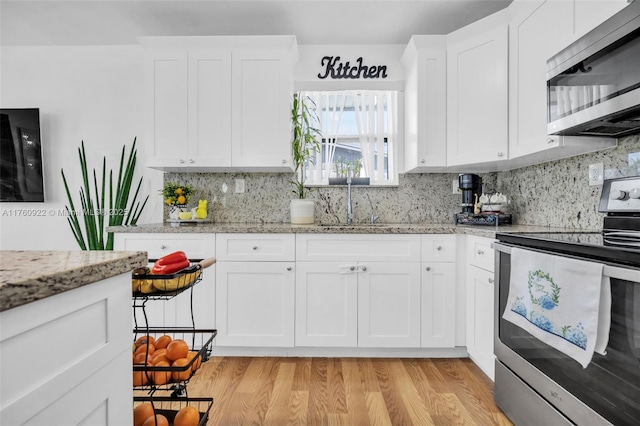 kitchen with light wood finished floors, a sink, white cabinets, appliances with stainless steel finishes, and tasteful backsplash