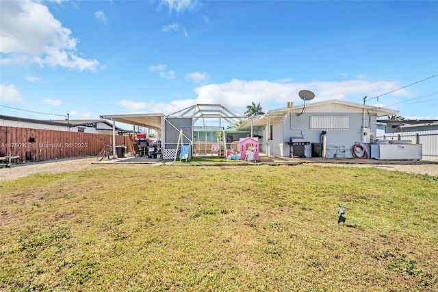 rear view of house featuring glass enclosure, a patio, a lawn, and a fenced backyard