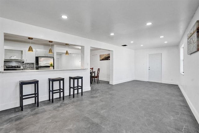 interior space with a breakfast bar, under cabinet range hood, refrigerator, recessed lighting, and white cabinets