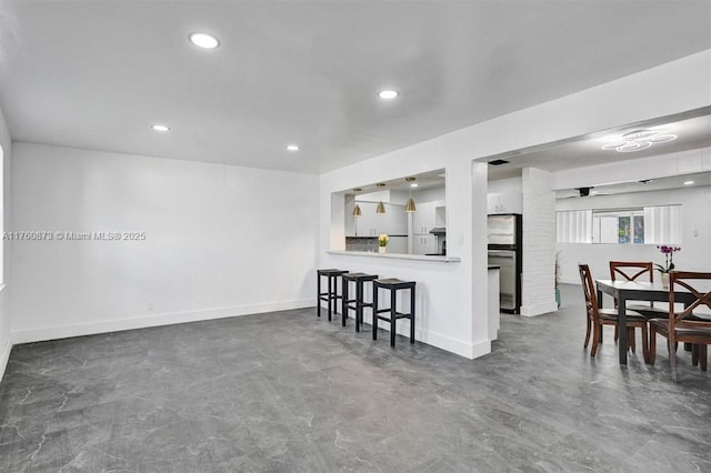 kitchen featuring recessed lighting, a kitchen bar, baseboards, and concrete flooring