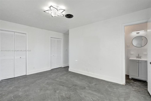 unfurnished bedroom with two closets, a sink, connected bathroom, baseboards, and concrete flooring