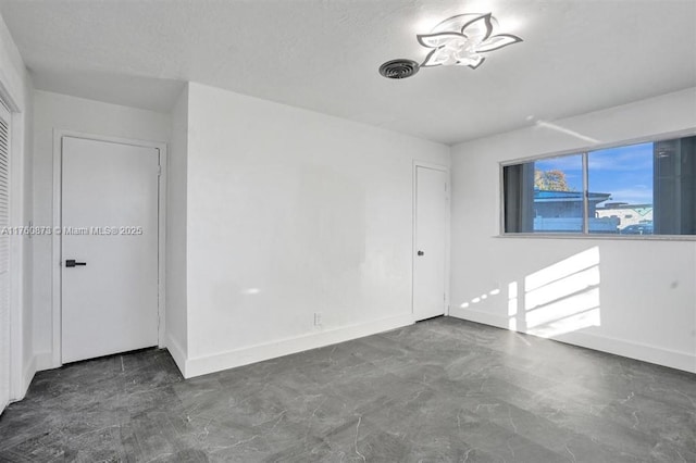 unfurnished room featuring baseboards, visible vents, and a textured ceiling