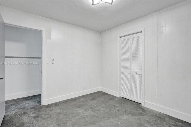 unfurnished bedroom with a closet, baseboards, and concrete flooring