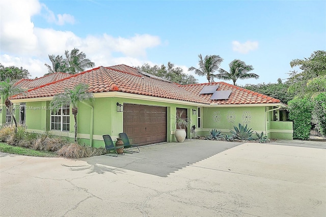 mediterranean / spanish-style house featuring stucco siding, a tile roof, concrete driveway, an attached garage, and solar panels