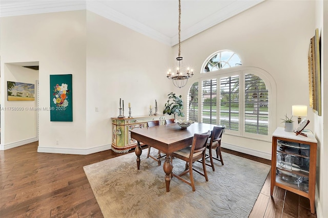 dining room featuring crown molding, baseboards, hardwood / wood-style floors, a towering ceiling, and an inviting chandelier