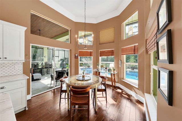 dining room with dark wood-style floors, baseboards, a towering ceiling, crown molding, and a chandelier