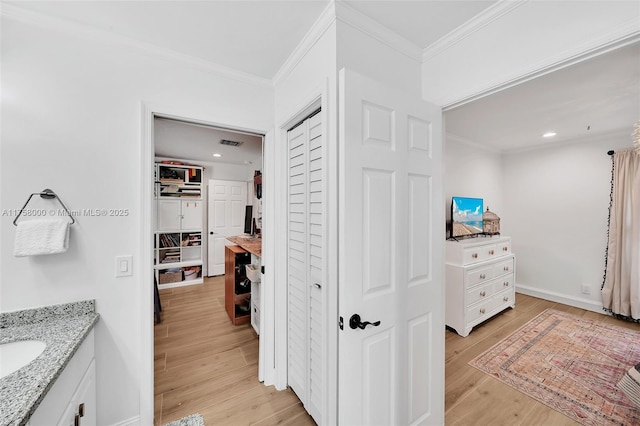 hall featuring visible vents, crown molding, light wood-type flooring, and baseboards