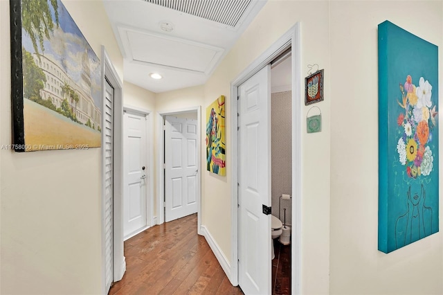 corridor with visible vents, baseboards, attic access, and wood finished floors