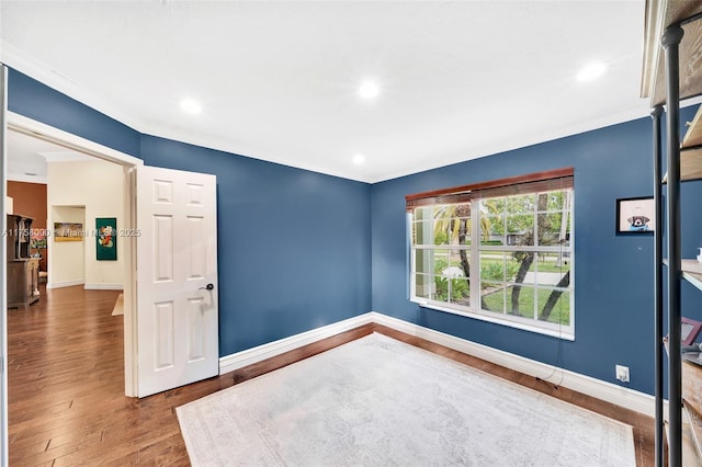 spare room with crown molding, wood finished floors, and baseboards