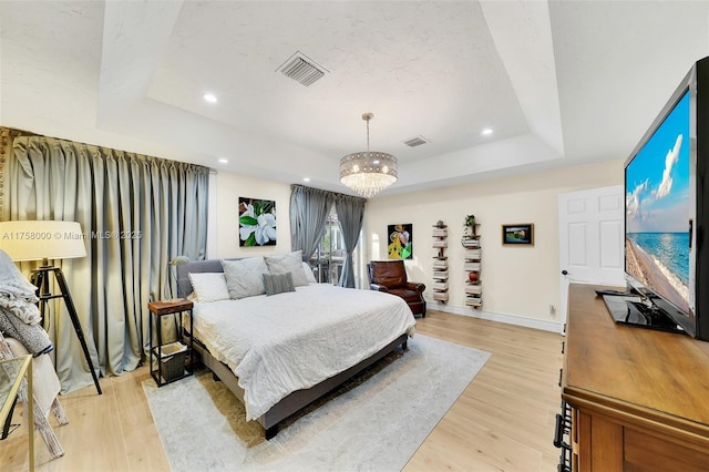 bedroom with light wood finished floors, visible vents, and a raised ceiling