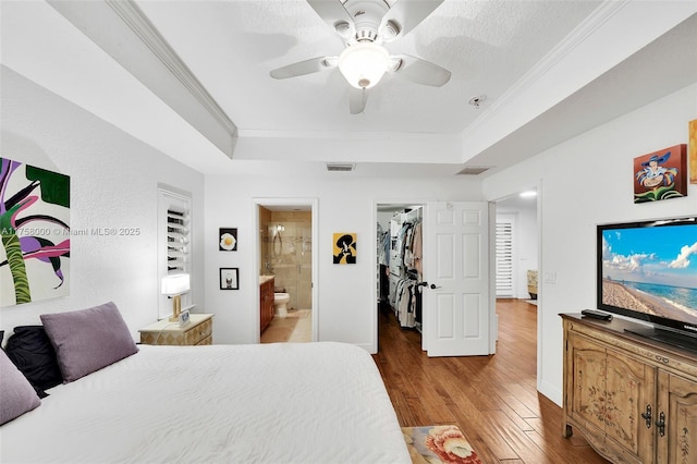 bedroom featuring wood finished floors, visible vents, a spacious closet, crown molding, and a raised ceiling