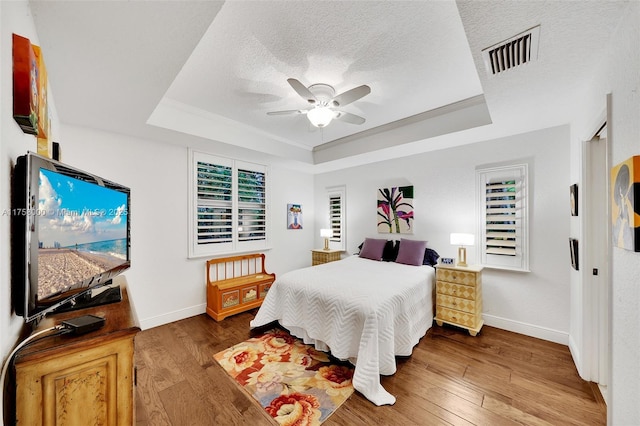 bedroom with visible vents, a textured ceiling, a tray ceiling, and hardwood / wood-style floors