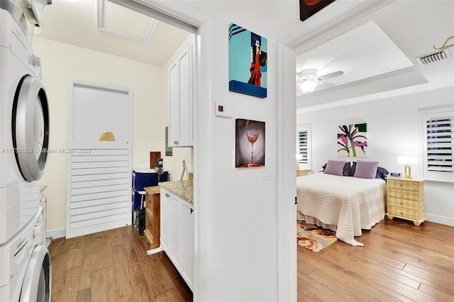 bedroom featuring visible vents, ceiling fan, attic access, hardwood / wood-style floors, and stacked washing maching and dryer