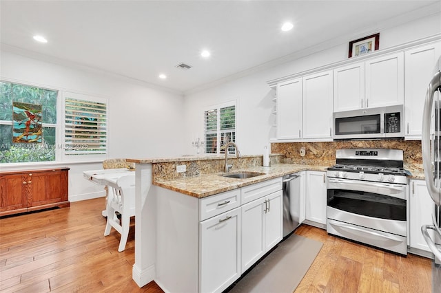 kitchen featuring visible vents, a peninsula, a sink, ornamental molding, and stainless steel appliances