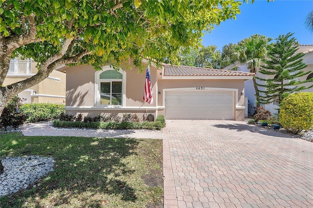 view of front facade featuring a tiled roof, stucco siding, an attached garage, and decorative driveway