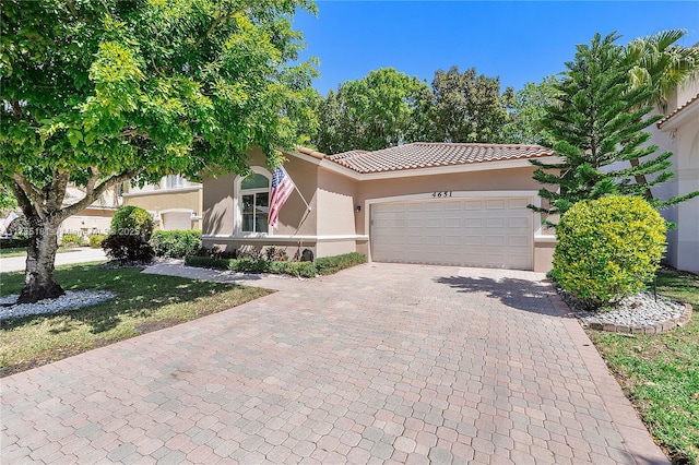 view of front of home featuring a tiled roof, stucco siding, an attached garage, and decorative driveway