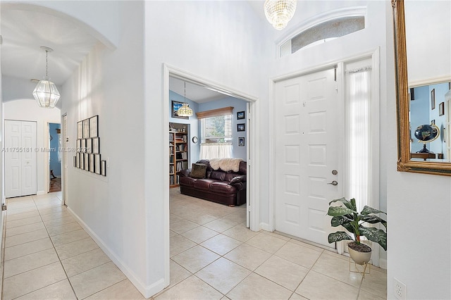 foyer with baseboards, light tile patterned floors, a high ceiling, an inviting chandelier, and arched walkways