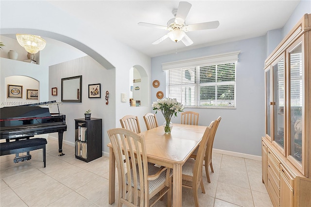 dining space featuring light tile patterned floors, baseboards, arched walkways, and a ceiling fan