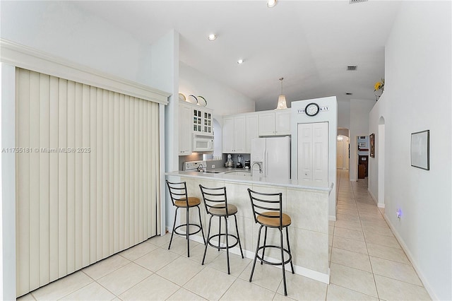 kitchen with white appliances, light tile patterned floors, a peninsula, arched walkways, and a kitchen bar