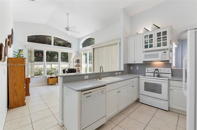 kitchen with white appliances, light tile patterned floors, a peninsula, and a sink