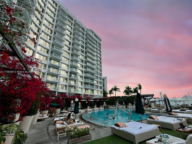 pool at dusk featuring a patio and a community pool