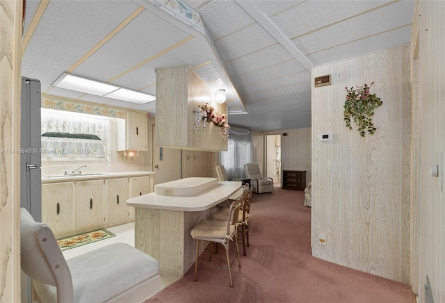 kitchen with light carpet, a sink, wooden walls, a breakfast bar area, and light countertops