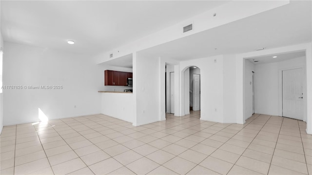 unfurnished room with arched walkways, light tile patterned floors, and visible vents