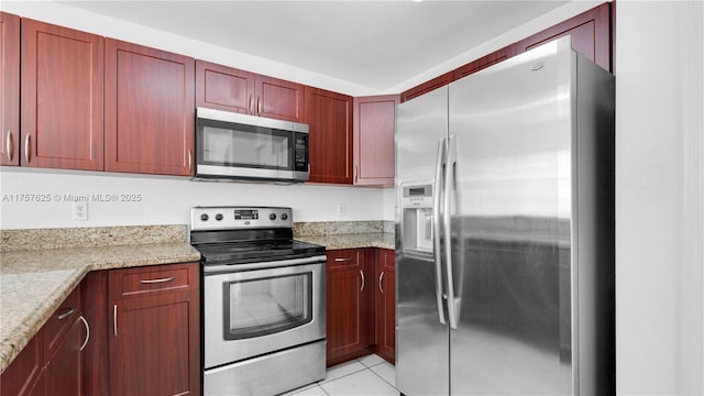 kitchen with light tile patterned floors, light stone countertops, stainless steel appliances, and reddish brown cabinets