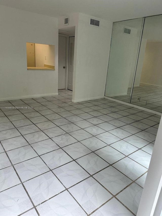 empty room with light tile patterned floors, visible vents, and baseboards