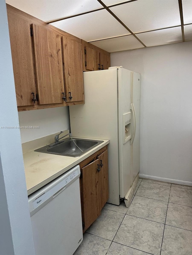 kitchen with light countertops, light tile patterned floors, brown cabinets, white appliances, and a sink