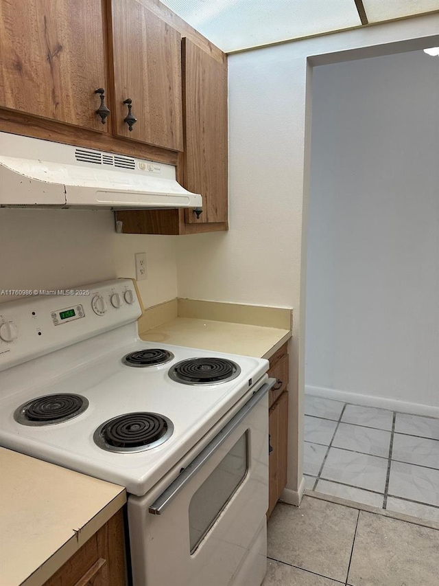 kitchen with baseboards, white range with electric cooktop, under cabinet range hood, light countertops, and brown cabinets