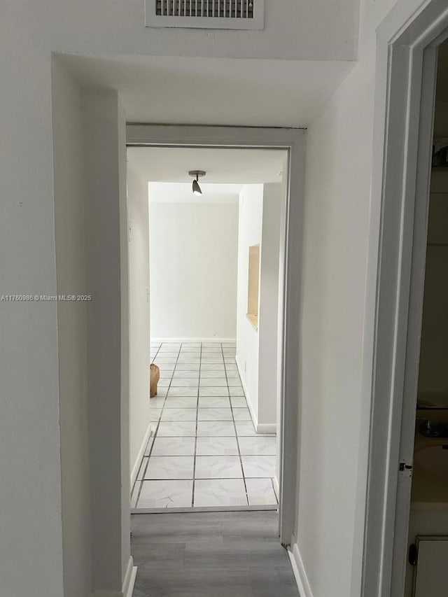 hallway with baseboards, visible vents, and marble finish floor