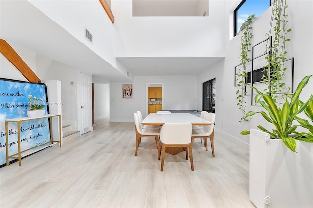 dining room with visible vents, baseboards, a high ceiling, and light wood-style flooring