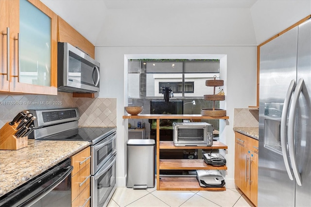 kitchen with decorative backsplash, light tile patterned floors, light stone countertops, and appliances with stainless steel finishes