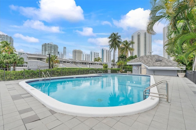 community pool with a patio area, a view of city, and fence